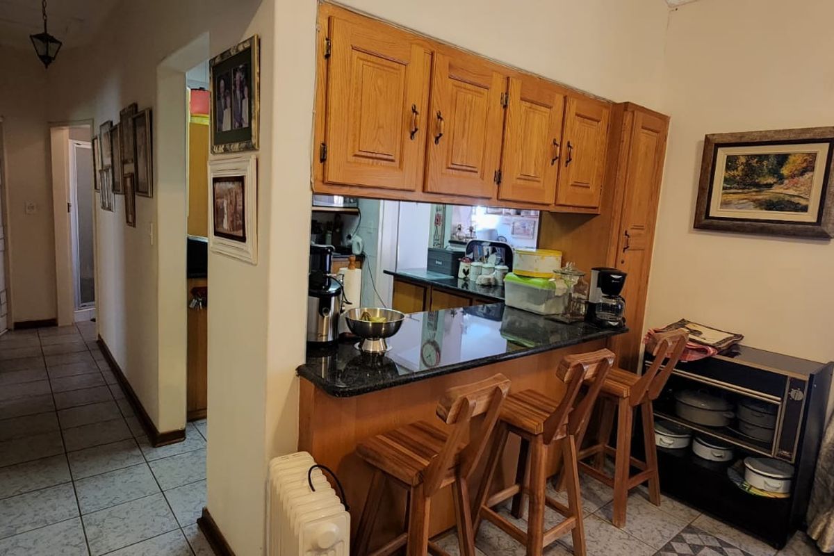 A kitchen area featuring wooden cabinetry, granite countertops, and a breakfast bar, connected to a tiled hallway.