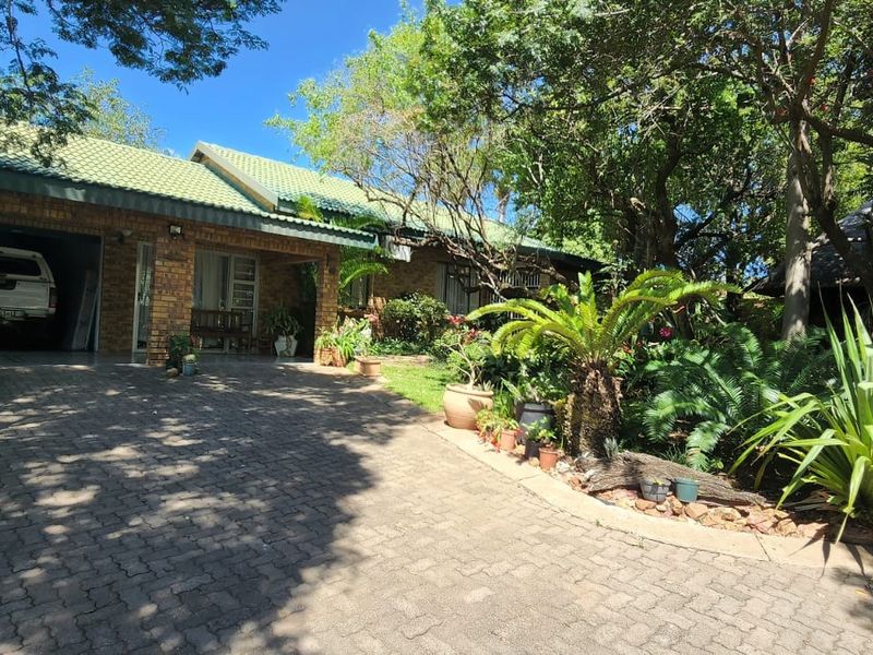 Front view of a brick house featuring a paved driveway, double garage, and established garden surroundings.
