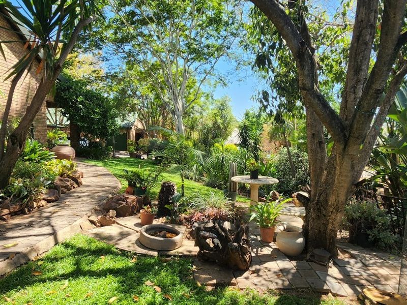A lush, well-established garden featuring mature trees, a paved walkway, and brick exterior wall, providing a serene outdoor space.