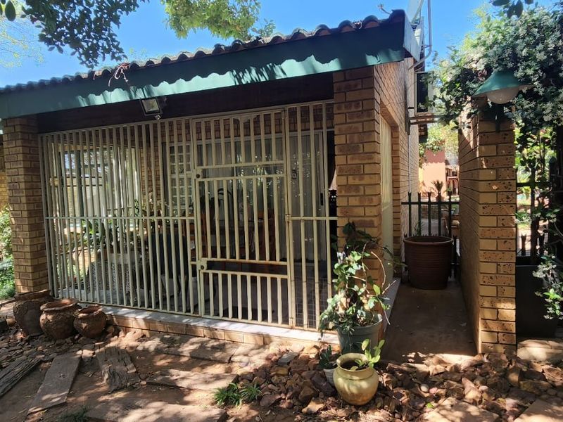 A covered outdoor patio area featuring brick construction, secure metal gating, and direct access to the surrounding garden space.