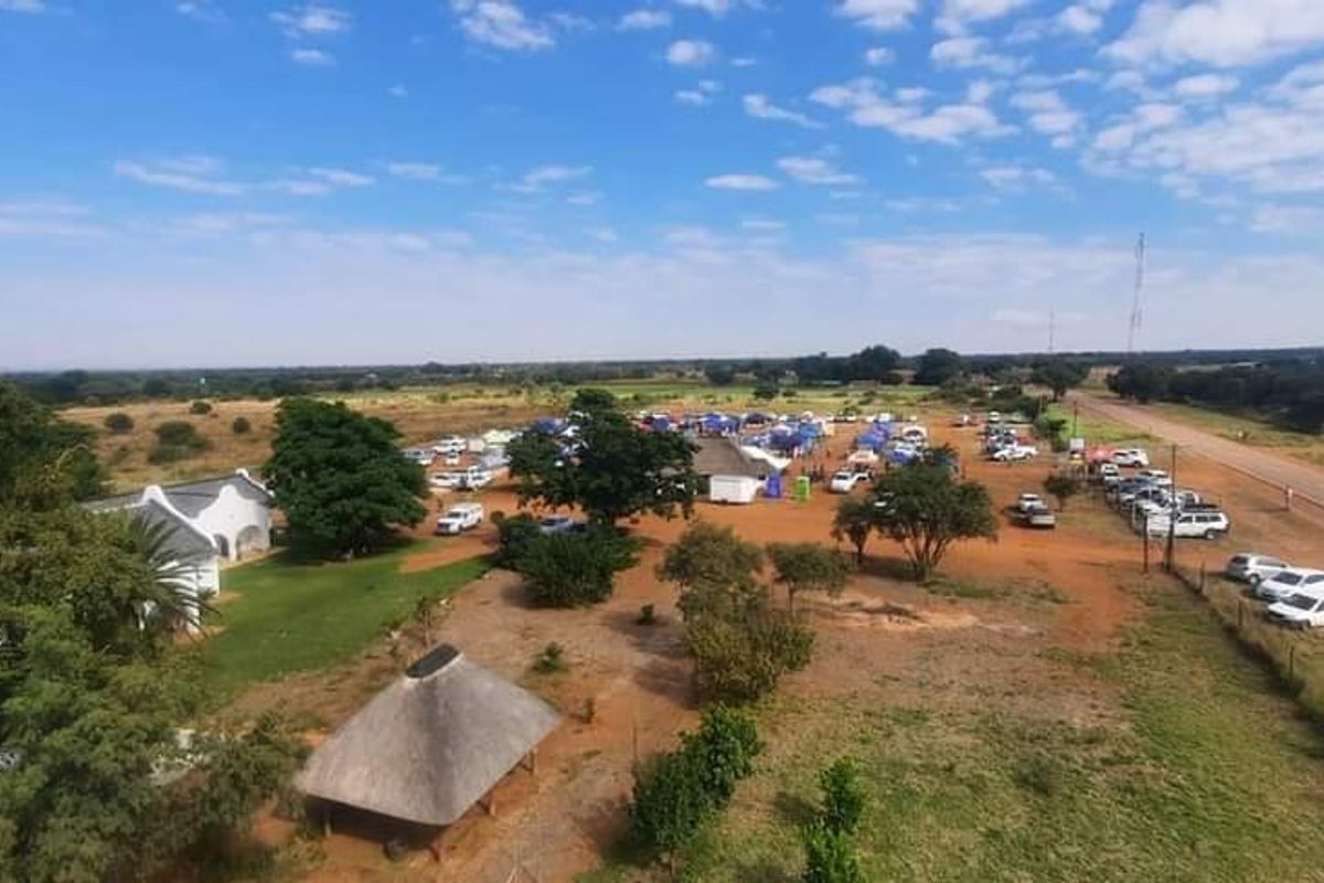 Aerial view of a small holding property featuring expansive grounds, a thatched roof structure, and direct access to the main road.