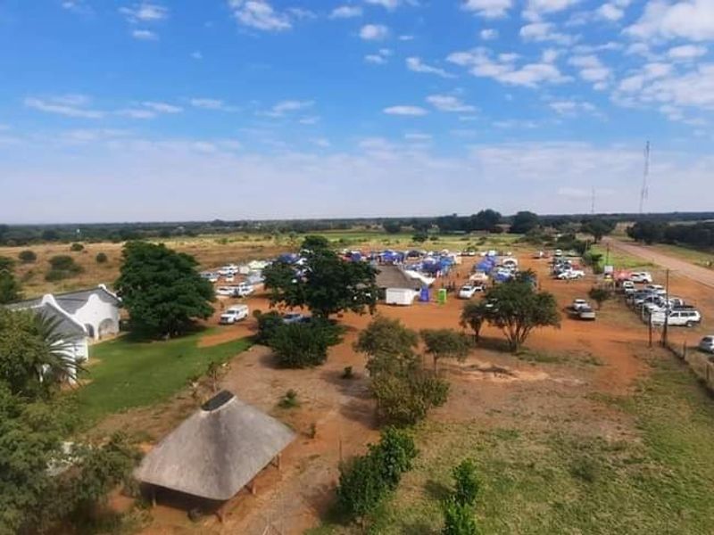 Aerial view of a small holding property featuring expansive grounds, a thatched roof structure, and direct access to the main road.