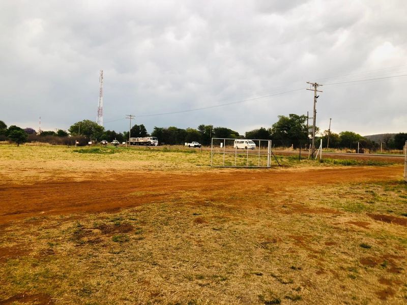 A view of the property entrance from the road, featuring a dirt driveway, wire fencing, and a metal gate.