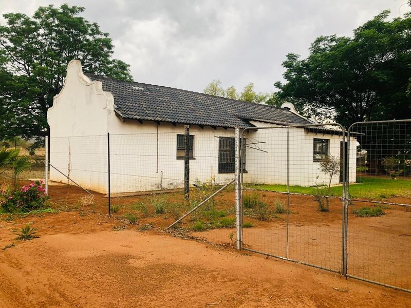 Rear view of a small holding dwelling featuring a gabled roof, security bars on windows, and enclosed by wire mesh fencing.