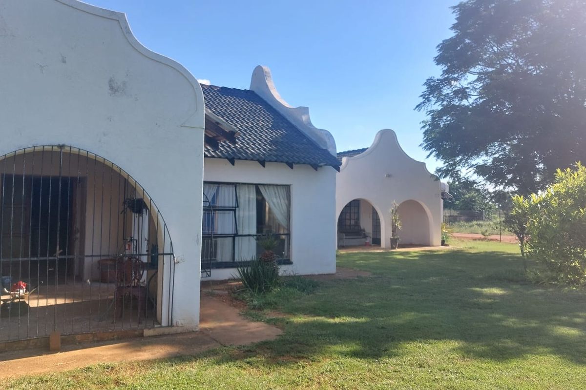 Rear view of a small holding property featuring traditional gabled architecture, arched patio areas, and a spacious garden.