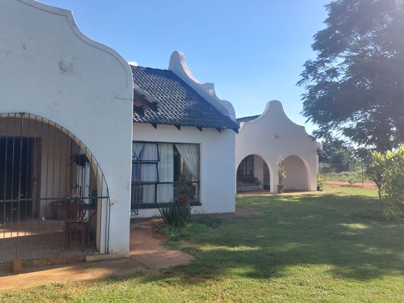 Rear view of a small holding property featuring traditional gabled architecture, arched patio areas, and a spacious garden.