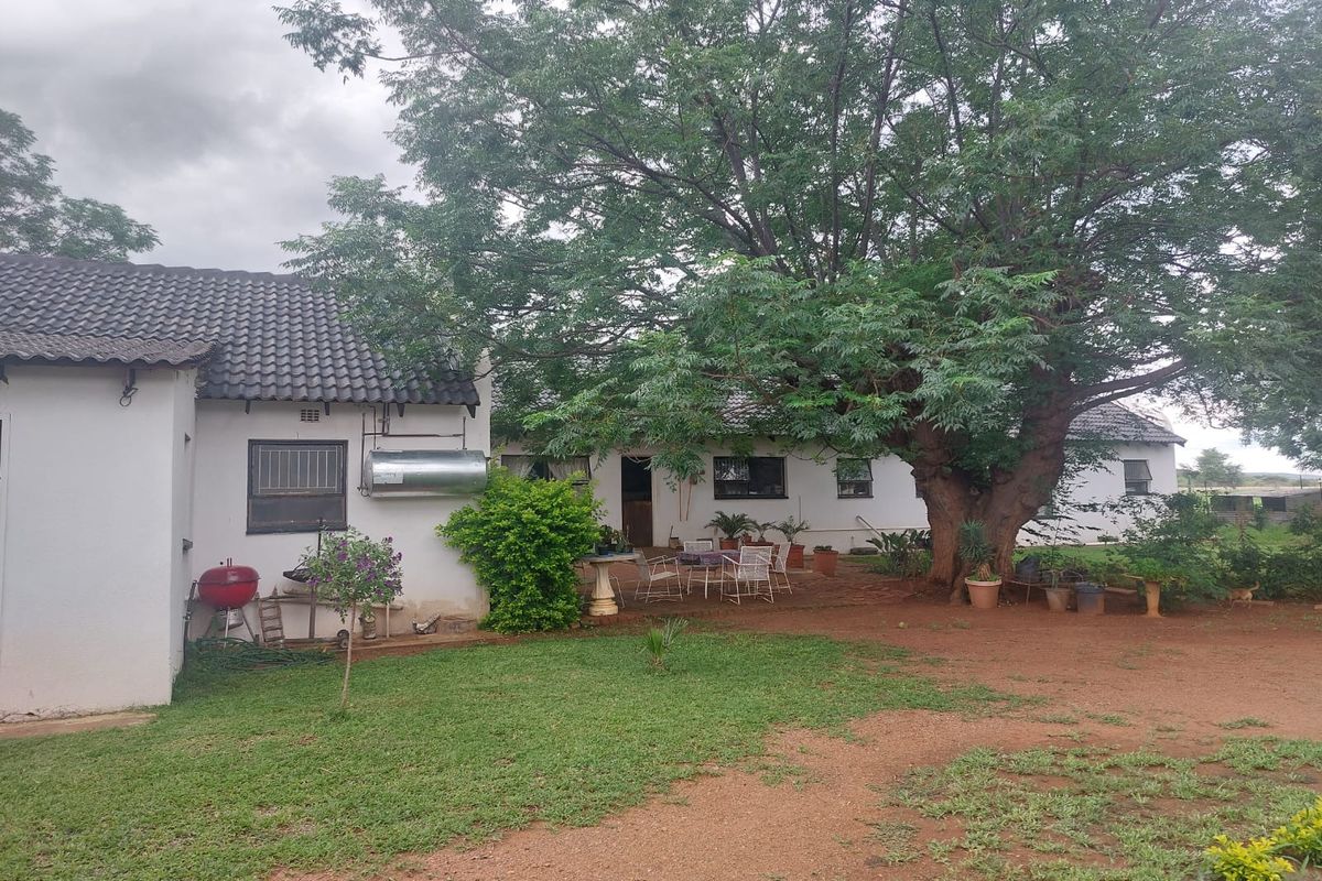 Rear view of the small holding dwelling featuring a tiled roof, solar geyser, and a spacious garden area with mature trees.