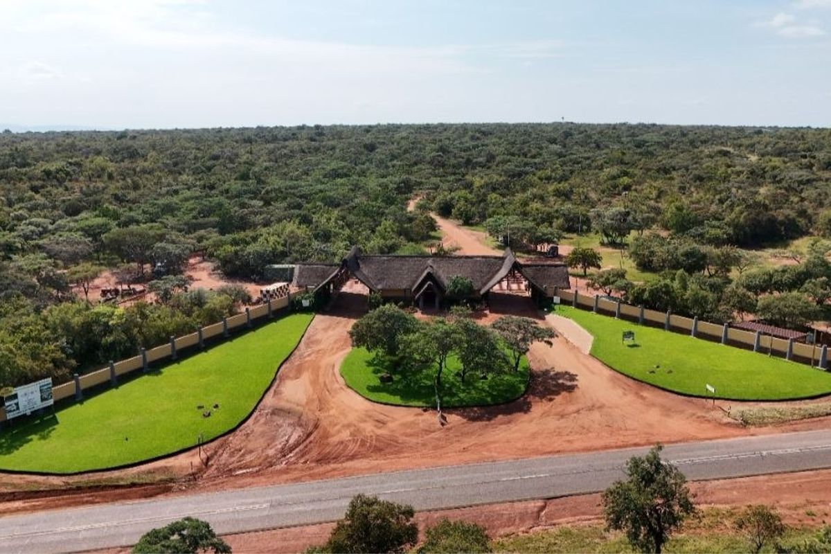 Aerial view of the property entrance featuring a thatched roof gatehouse, perimeter wall, and well-maintained landscaped grounds.