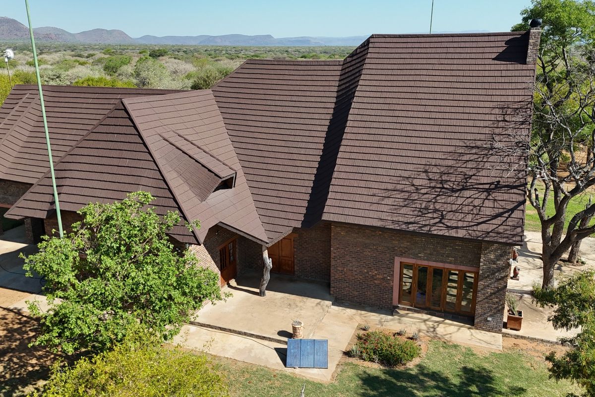 Aerial view of a brick farmhouse featuring a large tiled roof, surrounding patio area, and natural landscape setting.