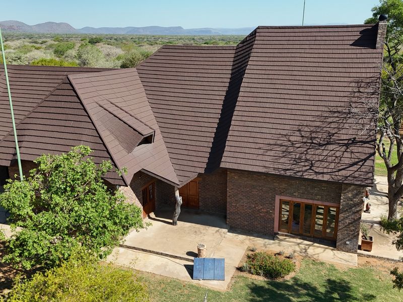 Aerial view of a brick farmhouse featuring a large tiled roof, surrounding patio area, and natural landscape setting.