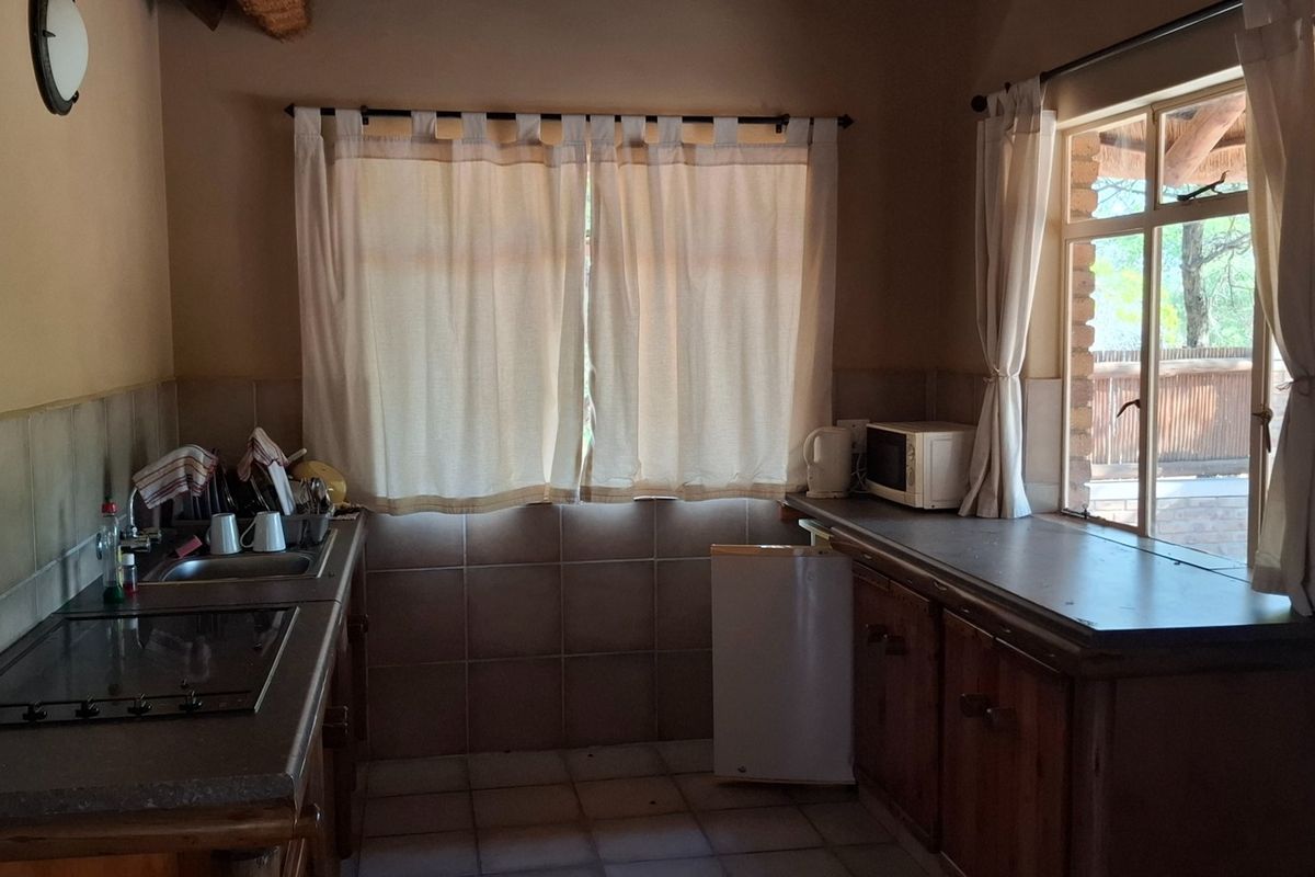 A functional kitchen featuring built-in wooden cabinetry, tiled splashbacks, a hob, and a sink, with natural light provided by a window.