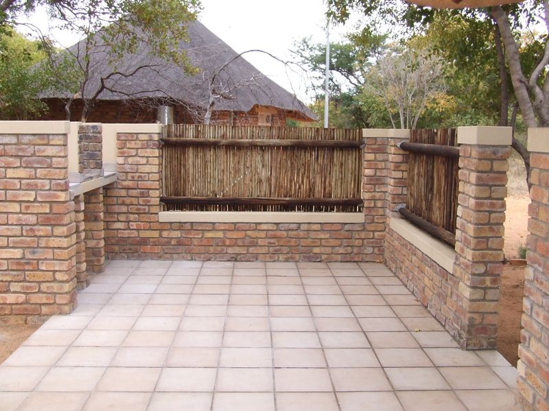 Outdoor patio area featuring a built-in brick braai, tiled flooring, and rustic timber screen fencing, set within a natural farm landscape.