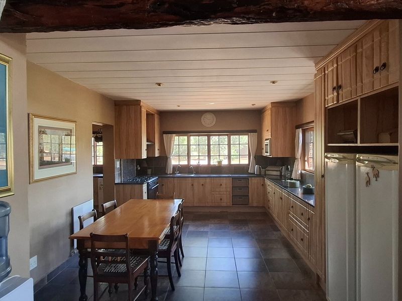 Spacious open-plan kitchen and dining area featuring warm wooden cabinetry, tiled floors, and a rustic exposed timber ceiling beam.