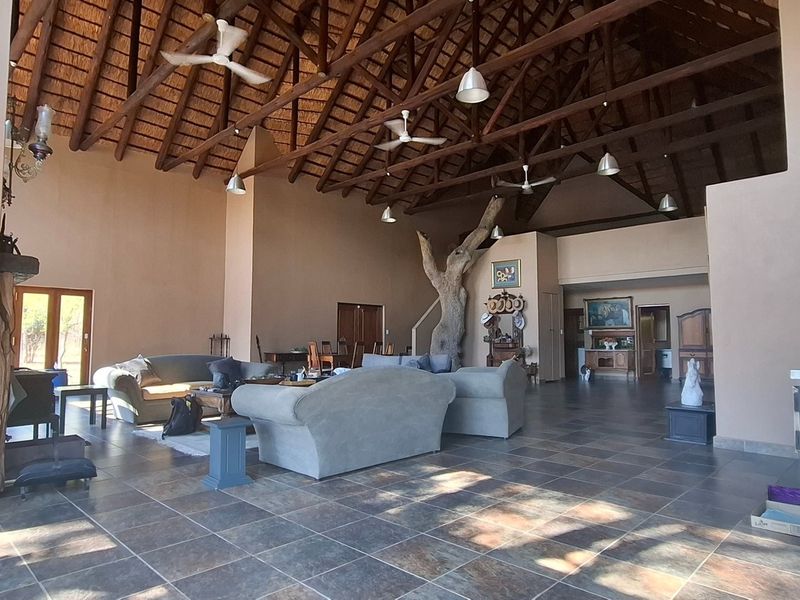 Spacious open-plan living area featuring a high vaulted thatched ceiling with exposed timber trusses, ceiling fans, and durable tiled flooring.