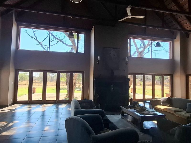 Spacious living room featuring a high vaulted timber ceiling with exposed trusses, tiled floors, a central fireplace, and expansive glass doors opening to the garden.