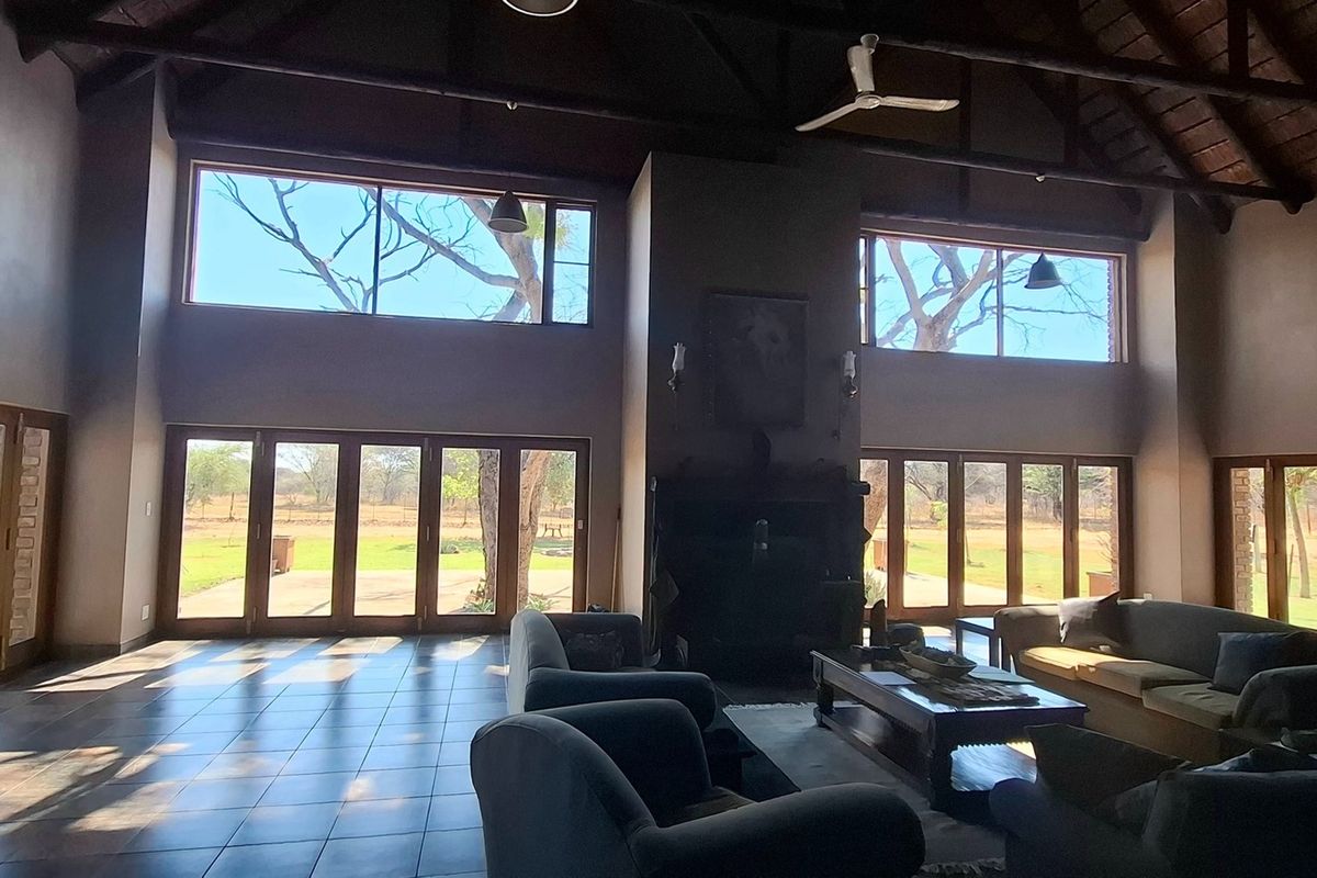 Spacious living room featuring a high vaulted timber ceiling with exposed trusses, tiled floors, a central fireplace, and expansive glass doors opening to the garden.