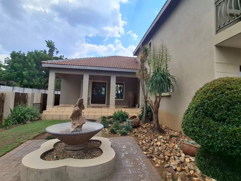 Rear exterior view featuring a covered patio, stone fountain, paved walkway, and landscaped garden area with a balcony above.