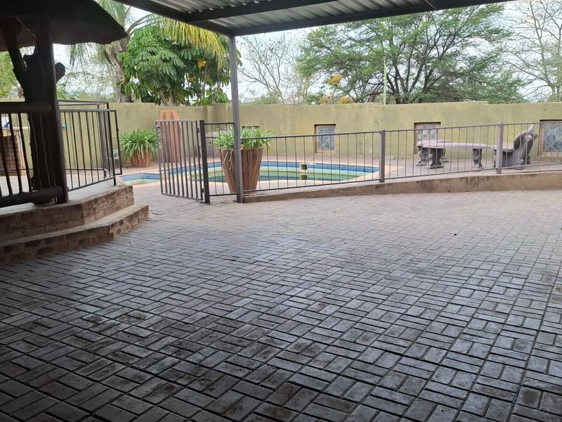 Outdoor entertainment area featuring a paved patio, covered section, and a swimming pool enclosed by metal safety fencing.