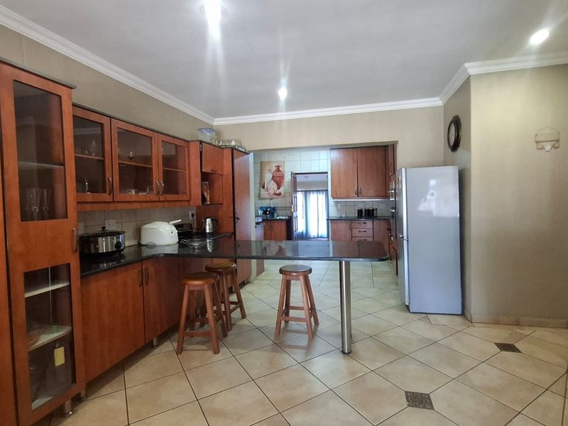 A functional kitchen featuring wooden cabinetry, granite countertops, a breakfast bar, and tiled flooring, with an open layout leading to a secondary prep area.