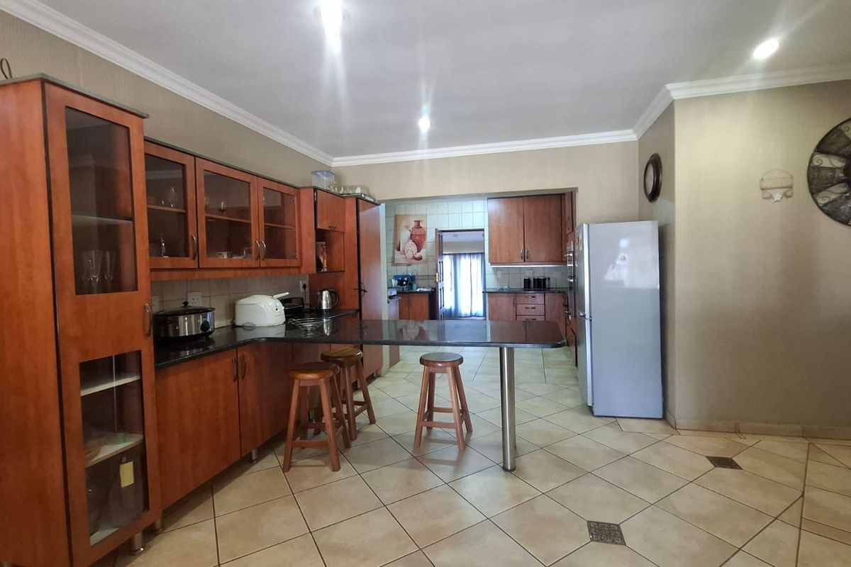A functional kitchen featuring wooden cabinetry, granite countertops, a breakfast bar, and tiled flooring, with an open layout leading to a secondary prep area.