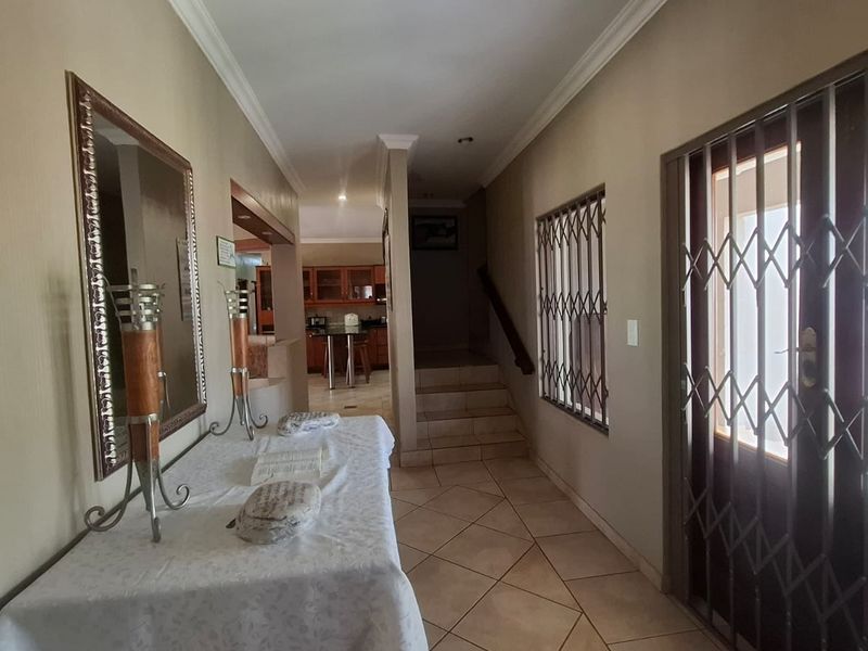 A spacious entrance hallway featuring tiled flooring, a staircase leading to the upper level, and a secure entrance door with metal security gate.