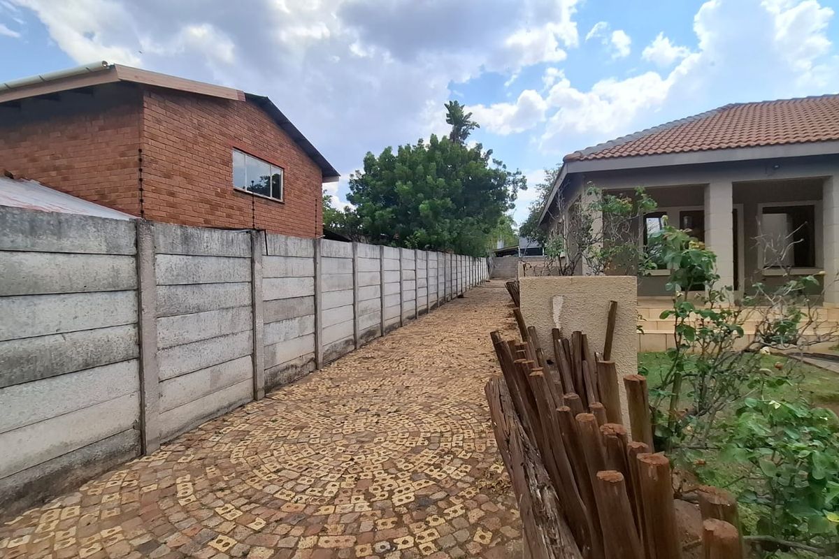 A rear exterior view showing a cobblestone pathway alongside a precast concrete boundary wall and a covered patio area.