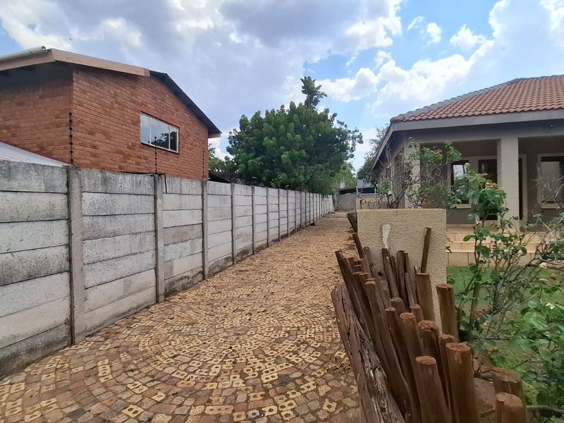 A rear exterior view showing a cobblestone pathway alongside a precast concrete boundary wall and a covered patio area.