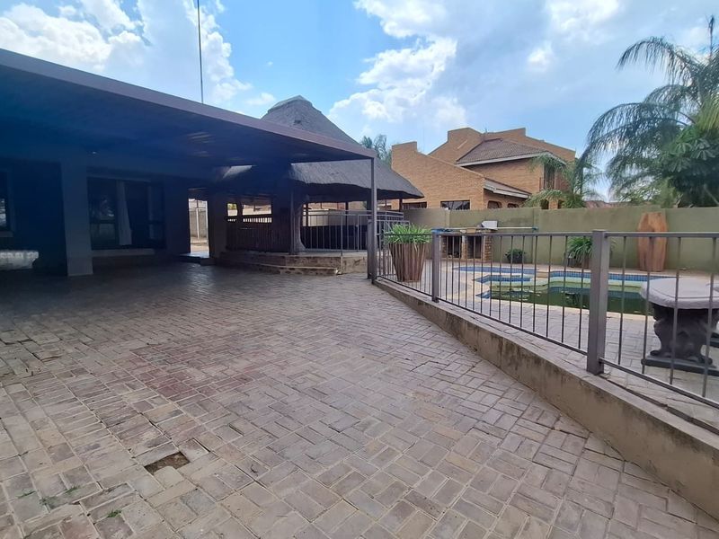 Spacious covered patio area featuring brick paving, a thatched lapa, and direct access to a swimming pool, offering potential for outdoor entertainment.