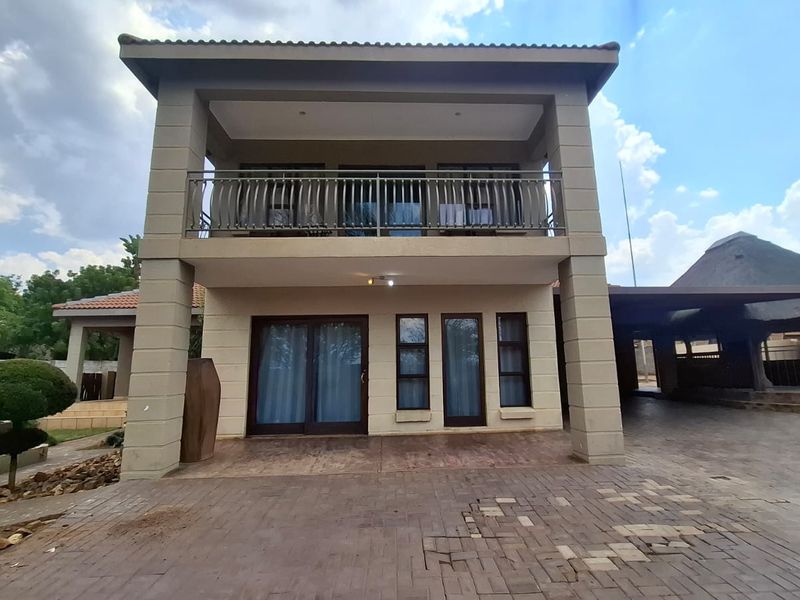 A two-story rear exterior view featuring a paved driveway, a ground-floor covered patio, and an upper-level balcony with metal railings.