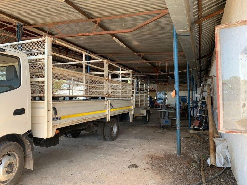 A large, open-sided farm shed or garage featuring a corrugated metal roof and steel support columns, suitable for vehicle storage or utility use.