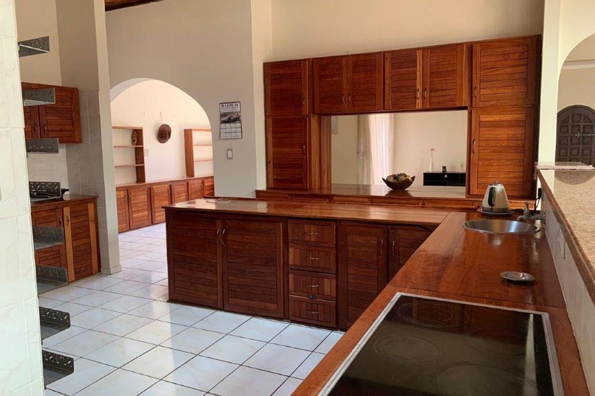 Spacious kitchen featuring extensive wooden cabinetry, a built-in hob, stainless steel sink, and tiled flooring with a classic archway leading to adjacent living areas.