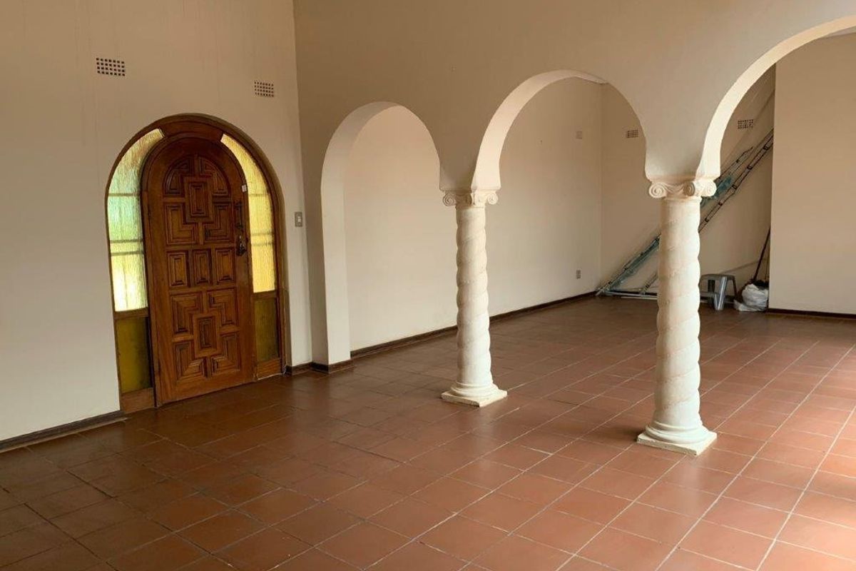 Spacious living area featuring classic arched architectural details, decorative columns, and durable tiled flooring, offering a blank canvas for interior design.