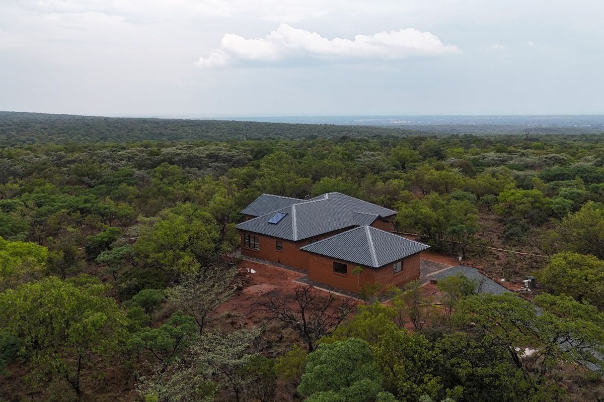 Aerial view of a detached brick house with a pitched roof, situated in a natural, wooded landscape.