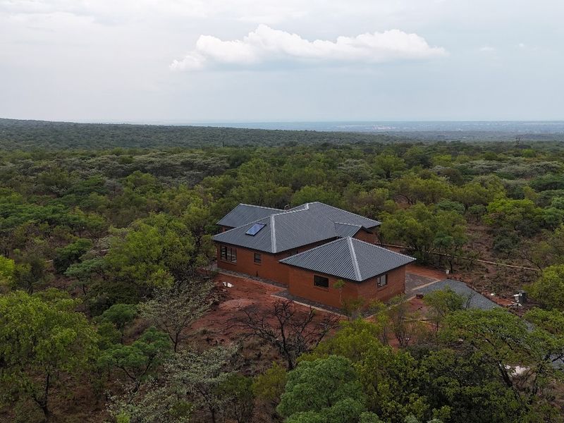 Aerial view of a detached brick house with a pitched roof, situated in a natural, wooded landscape.
