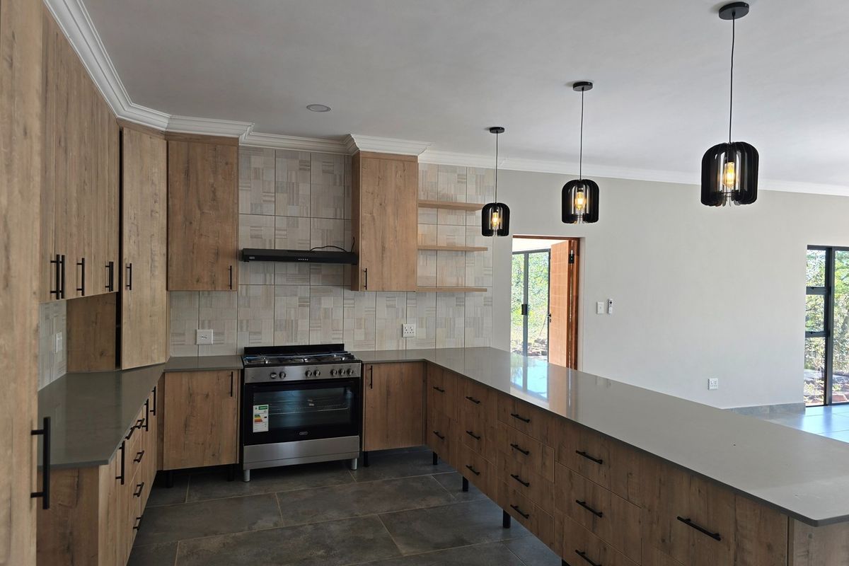 Modern kitchen featuring wood-finish cabinetry, stone countertops, a gas stove with extractor, and stylish pendant lighting, offering a clean and functional workspace.