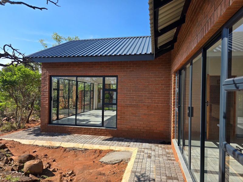 A modern face brick home exterior featuring large aluminium sliding doors, a corrugated metal roof, and a paved walkway leading to an outdoor patio area.