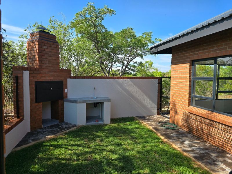 Outdoor patio area featuring a built-in brick braai, concrete prep counter with sink, and paved flooring adjacent to the main house structure.