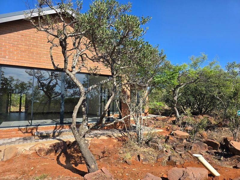 A modern house exterior featuring exposed brickwork and large glass sliding doors opening onto a natural, rocky garden setting.