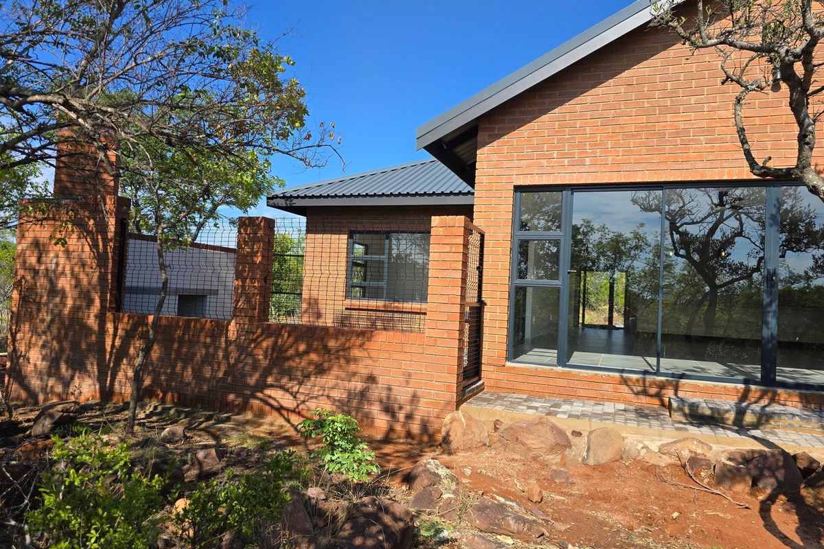 Rear view of a modern face brick house featuring large sliding glass doors, a metal roof, and a paved patio area.