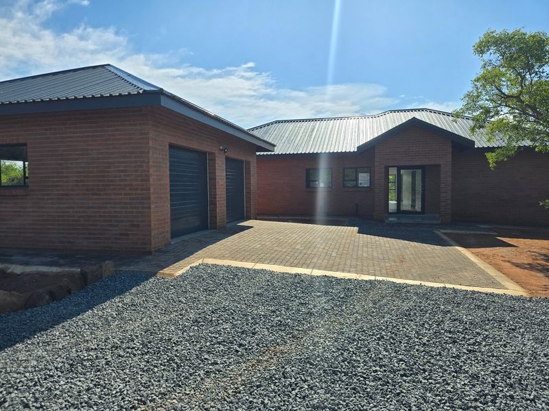 A modern single-story brick house featuring a double garage, metal roofing, and a paved driveway leading to the main entrance.