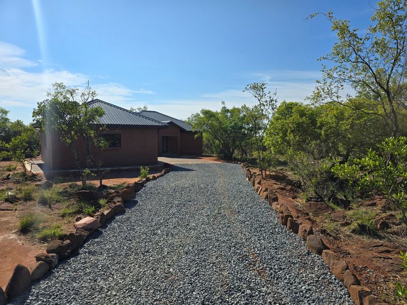 A view of the front exterior of a brick house featuring a metal roof and a gravel driveway leading to the entrance.