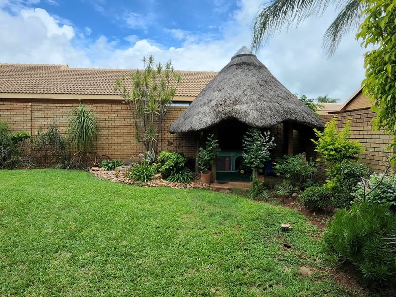 A private rear garden featuring a traditional thatched lapa, established landscaping, and a brick boundary wall, providing a peaceful outdoor space.