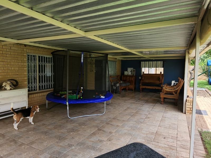 A covered outdoor patio area featuring tiled flooring, brick walls, and security bars, providing a functional space for outdoor living and entertainment.