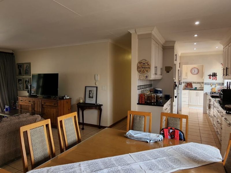 Open-plan living and dining area flowing into a functional kitchen with built-in cabinetry and tiled finishes, leading out to a covered patio.