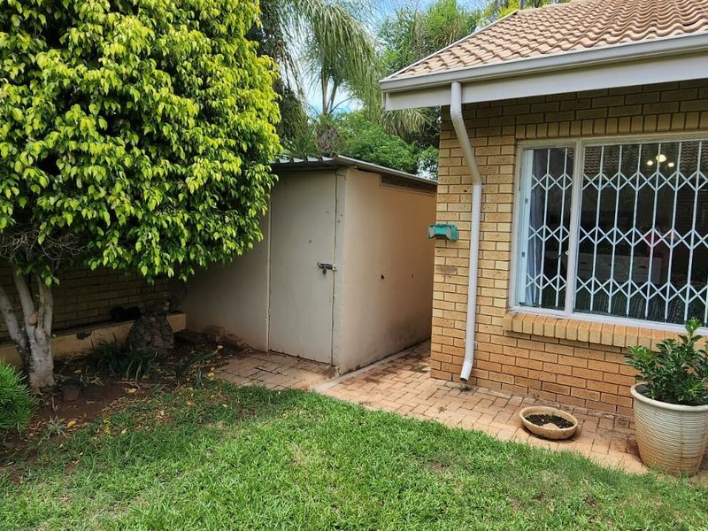 Rear exterior view of the townhouse featuring a brick facade, security window bars, a paved walkway, and a detached metal storage shed.