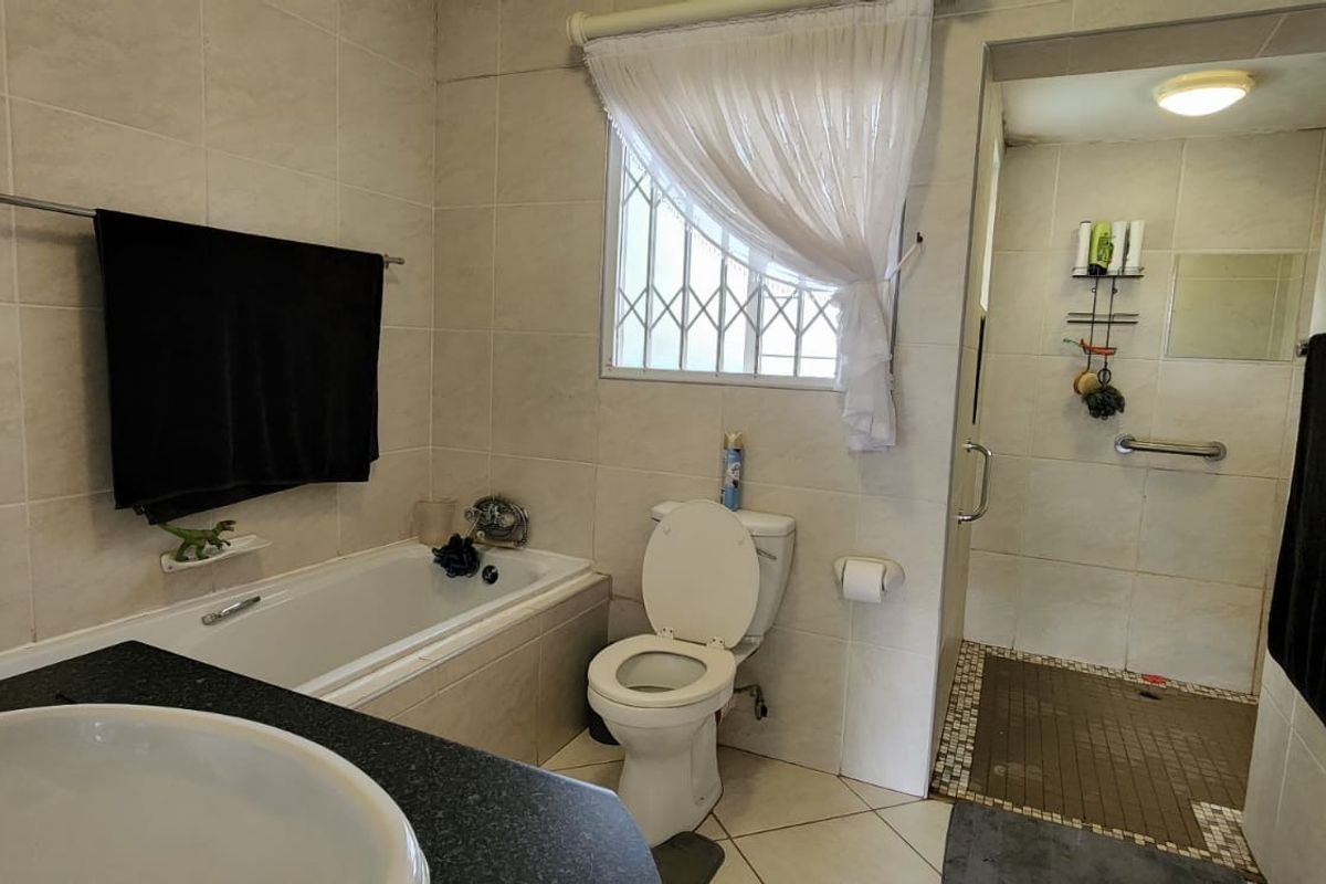 A functional bathroom featuring a built-in bathtub, separate walk-in shower, vanity basin, and tiled finishes throughout.