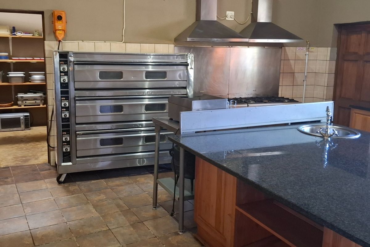 Commercial-style kitchen featuring a multi-deck oven, stainless steel extractor hoods, granite countertops, and a convenient walk-in pantry for ample storage.