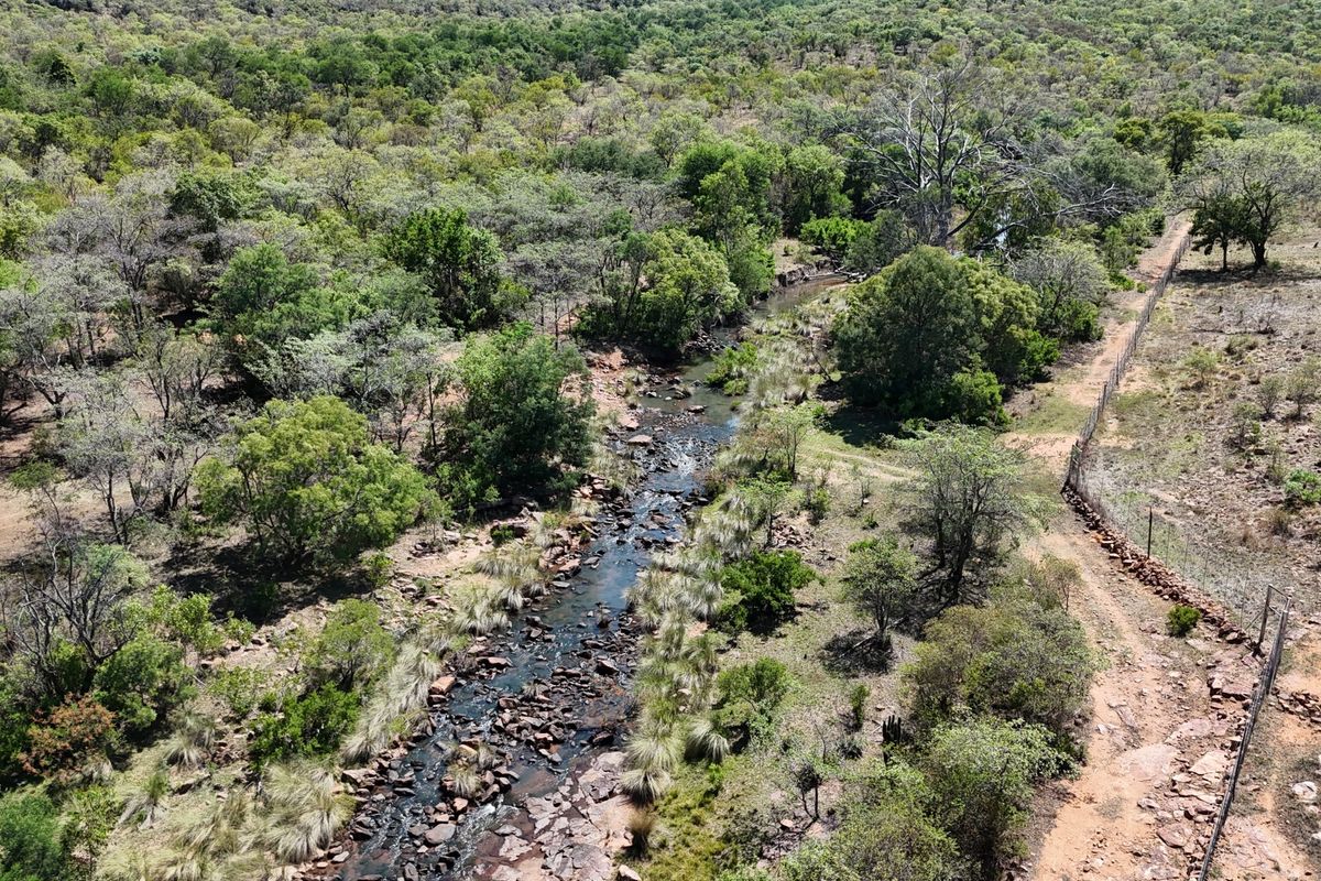 An aerial view of the farm property featuring a natural flowing stream, surrounding indigenous vegetation, and perimeter fencing.