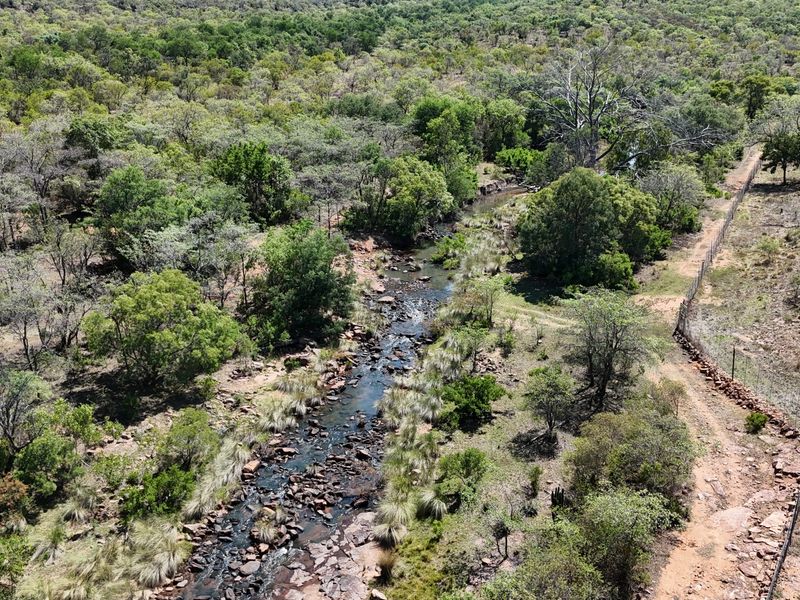 An aerial view of the farm property featuring a natural flowing stream, surrounding indigenous vegetation, and perimeter fencing.
