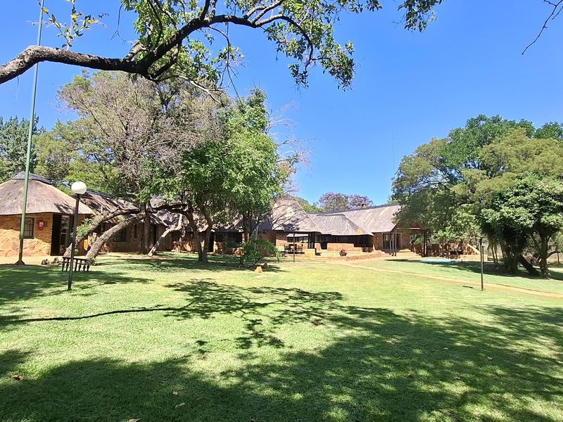 A spacious farm property featuring multiple structures with traditional thatched roofs and stone masonry walls, set within a well-maintained garden with mature trees.